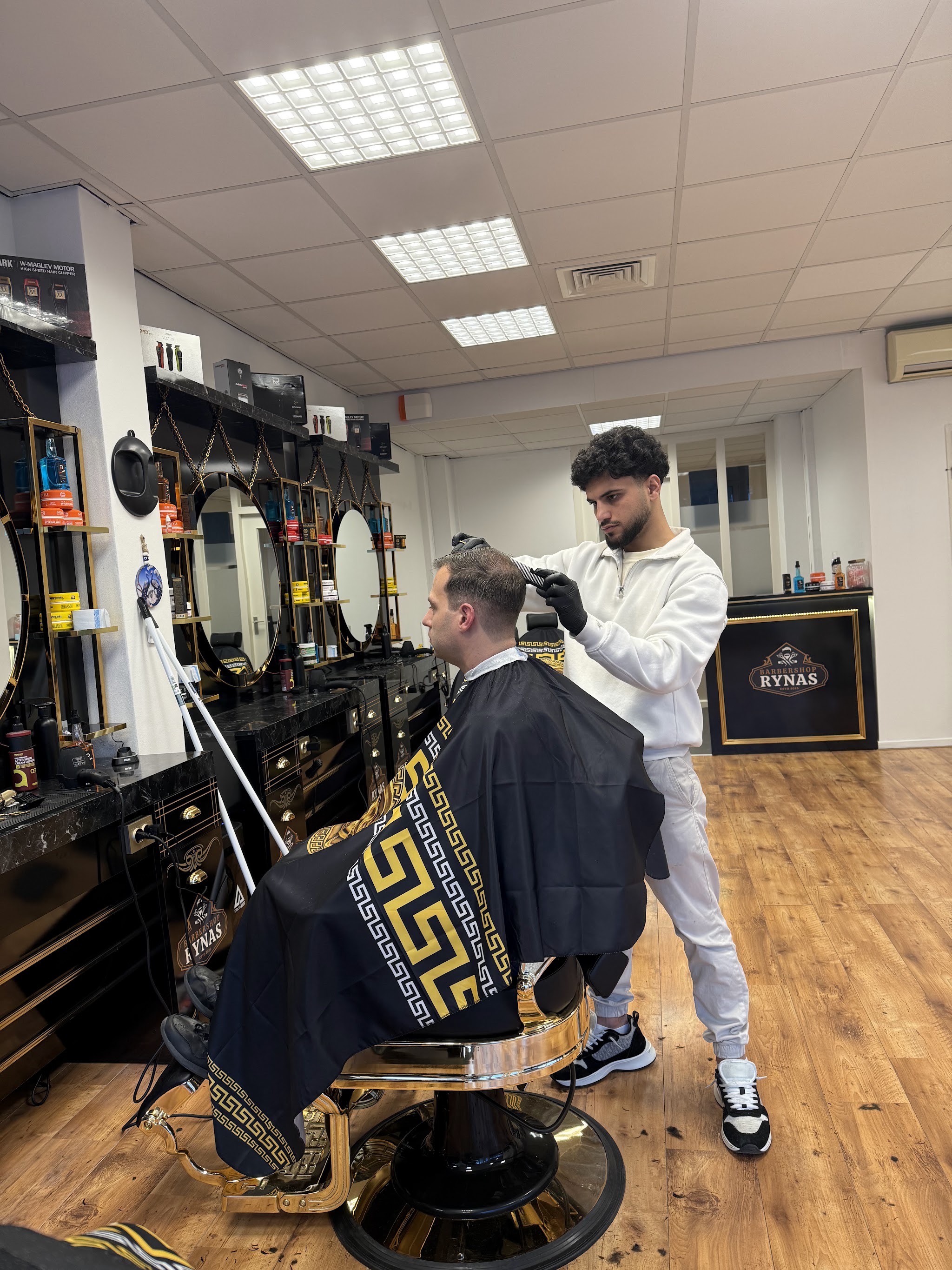 Een barbier aan het werk in Barbershop Rynas, met het wapenlogo aan de muur